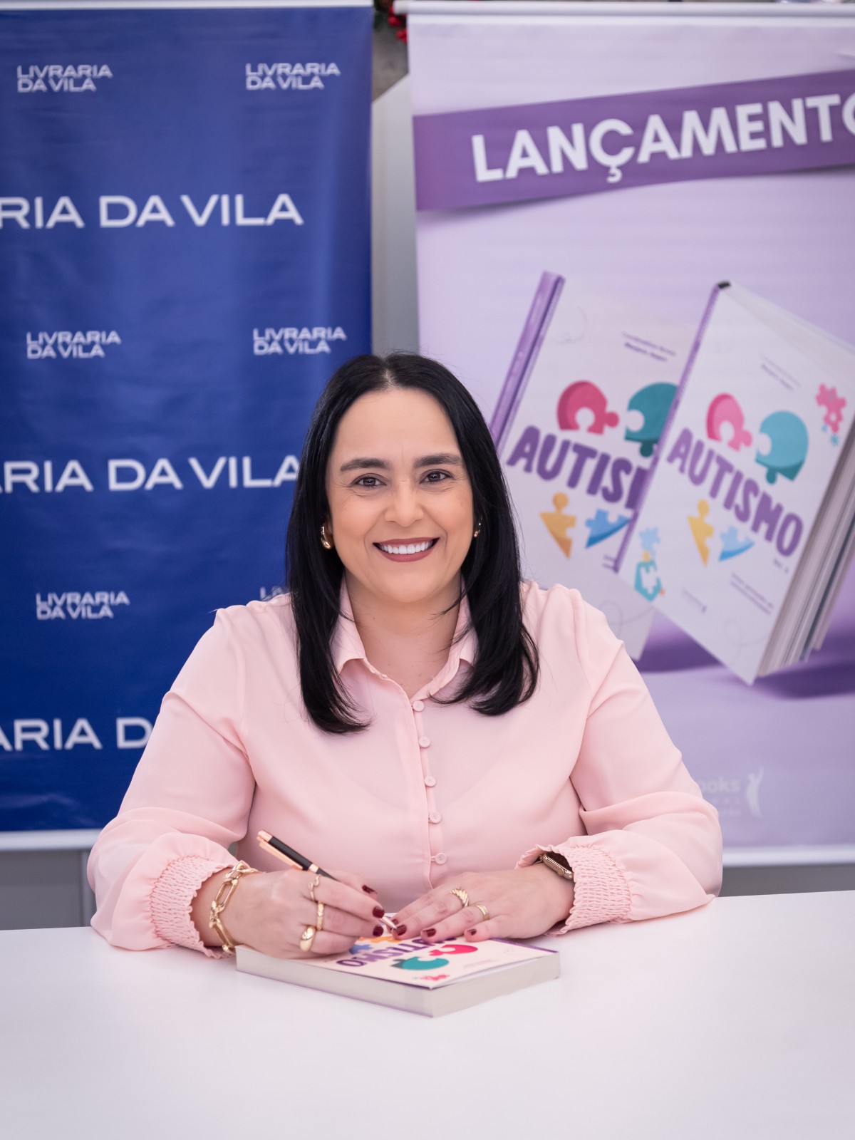 Patrícia Bastos em sessão de autógrafos, com o banner “Lançamento do livro”