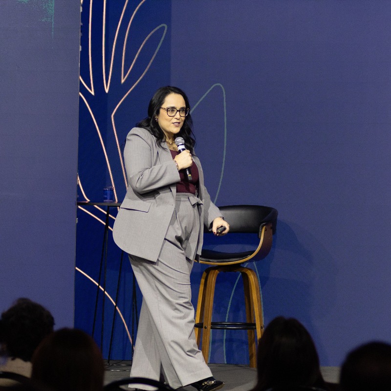 Patrícia Bastos no palco, de microfone, diante da plateia